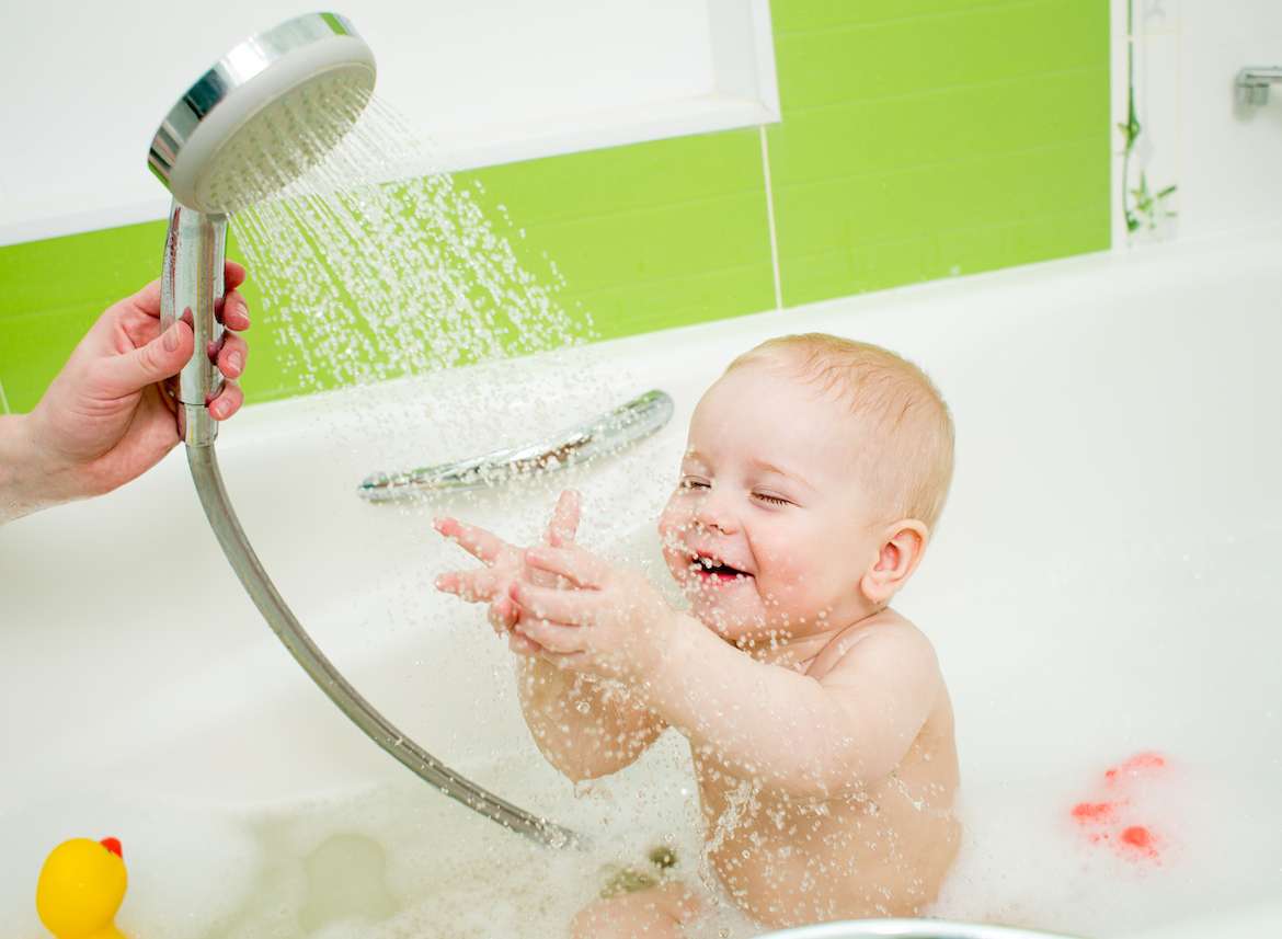 A mom holding a shower while bathing her baby in the bathtub