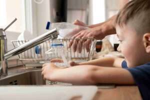 A boy filling a water bottle in a running kitchen faucet