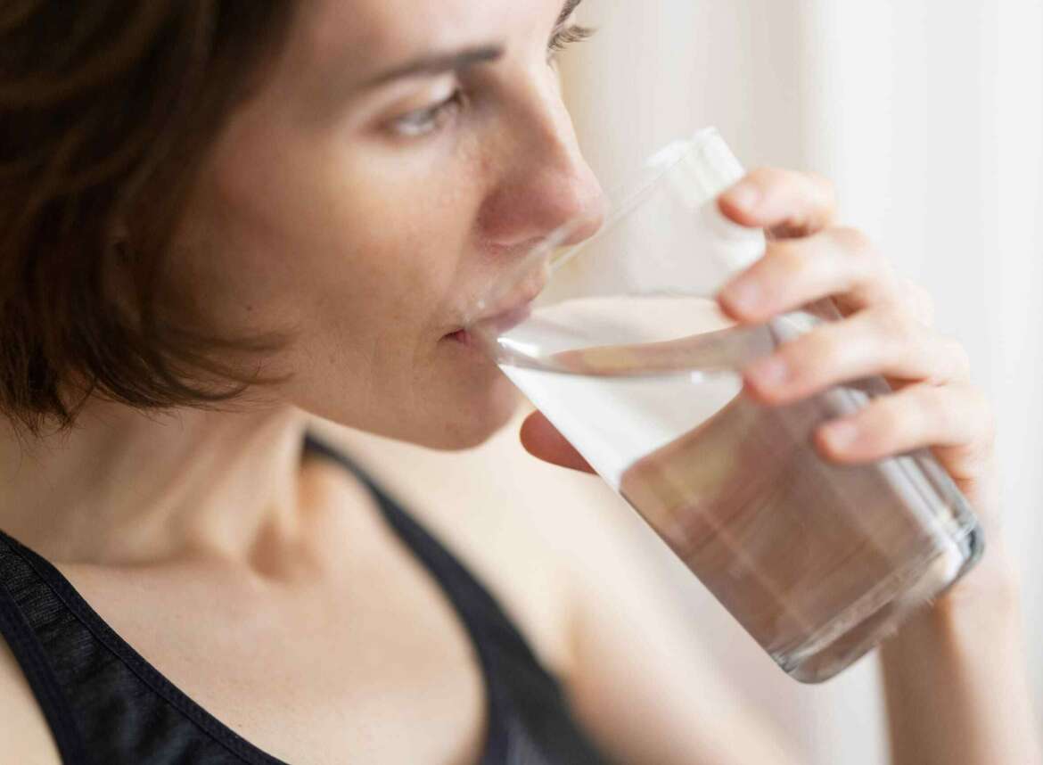 A woman in black tank top drinking a glass of filtered water