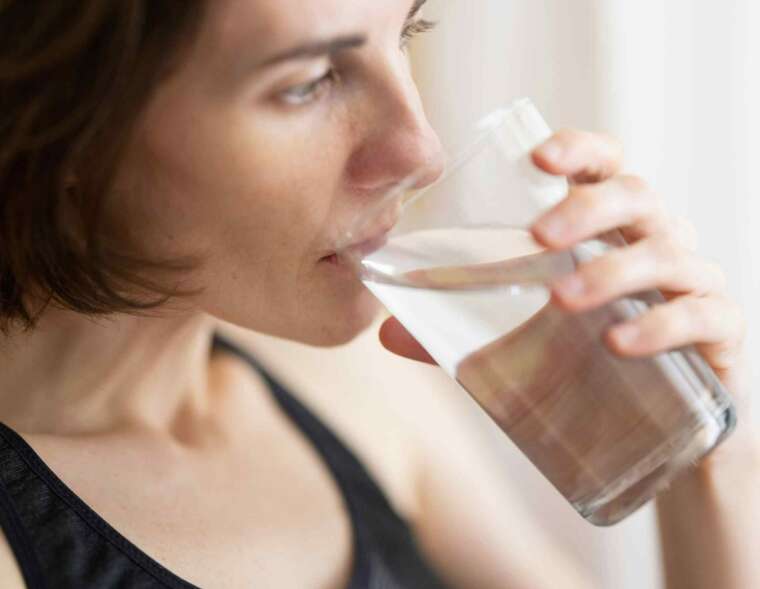 A woman in black tank top drinking a glass of filtered water