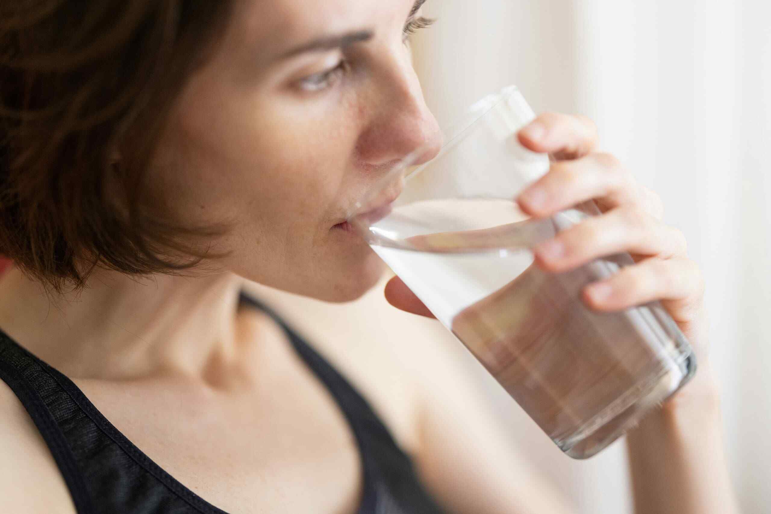 A woman in black tank top drinking a glass of filtered water