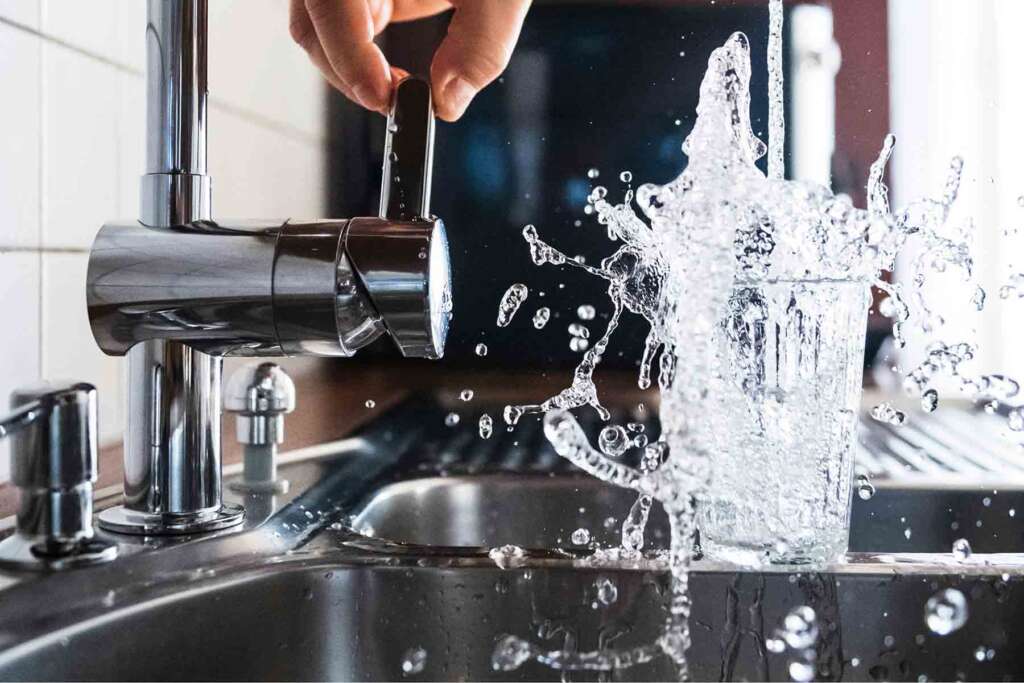 A person turns on a faucet, filling a glass with water