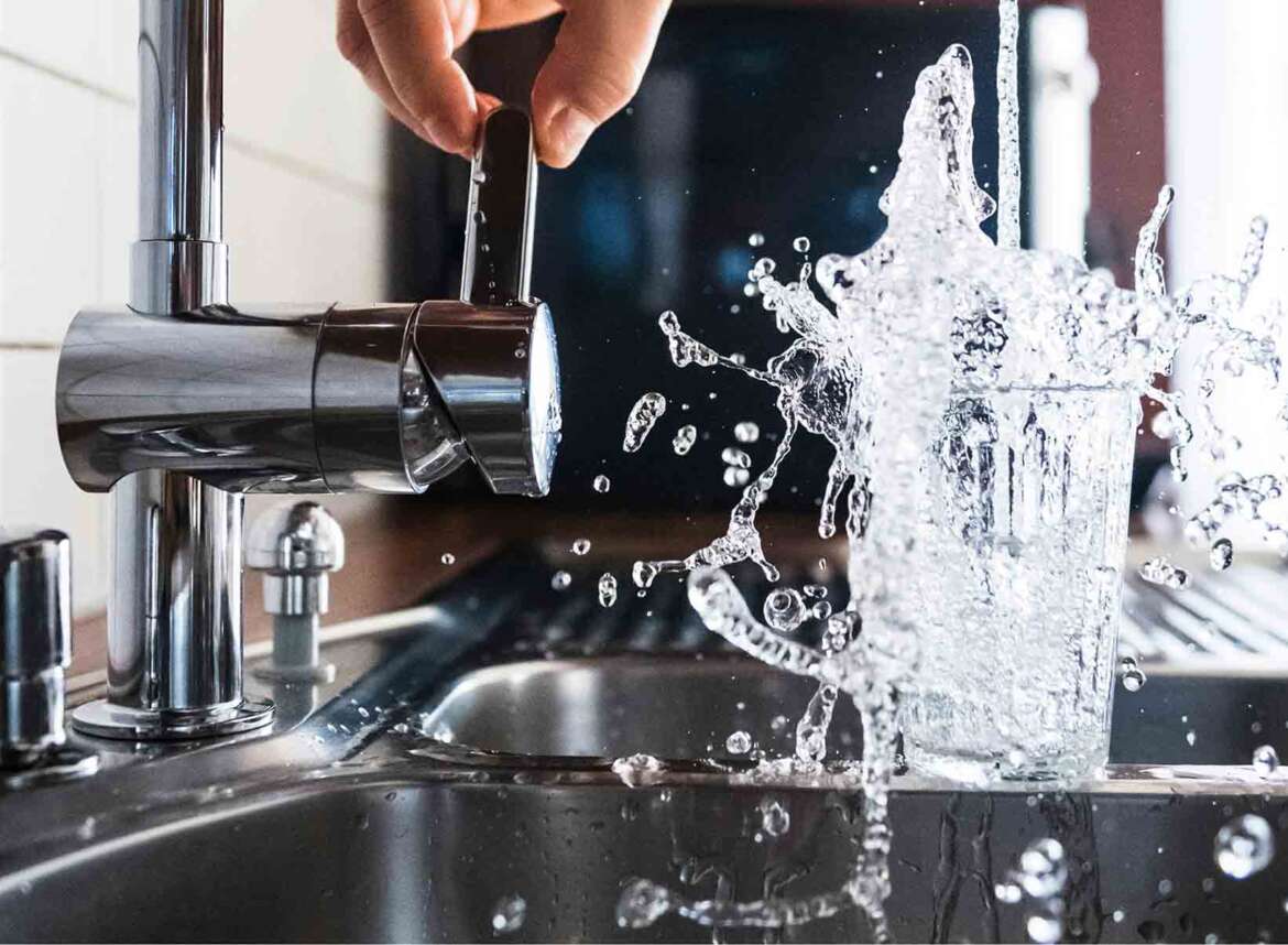 A person turns on a faucet, filling a glass with water