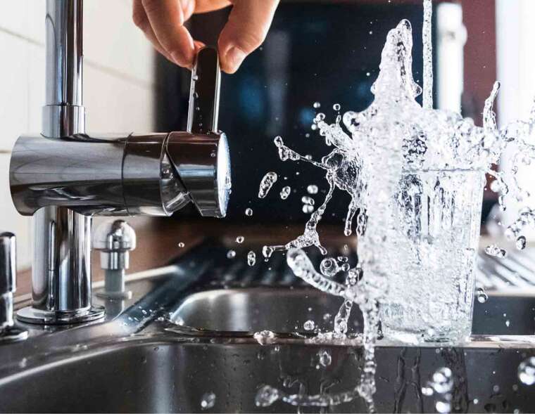 A person turns on a faucet, filling a glass with water