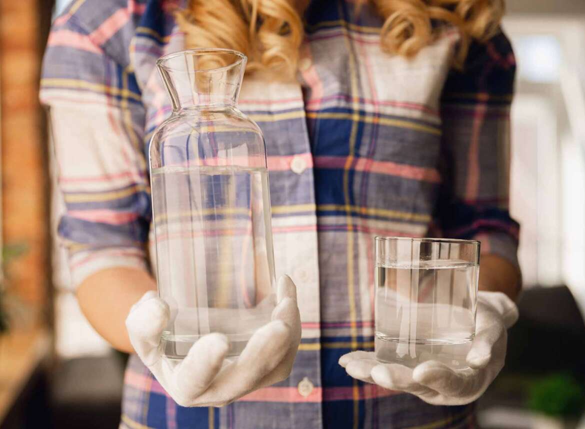 A woman holding a pitcher with unfiltered water and a glass of water