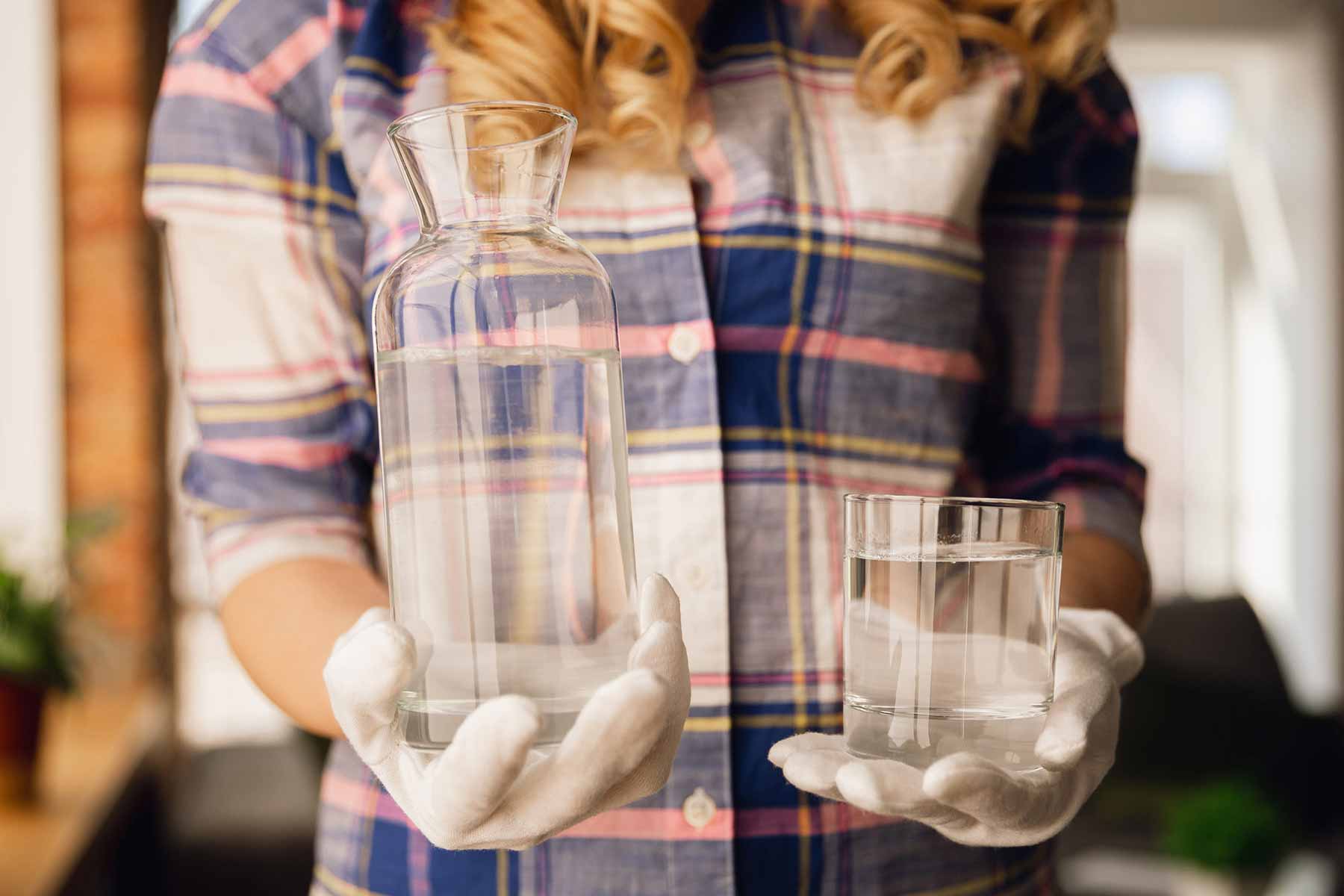 A woman holding a pitcher with unfiltered water and a glass of water