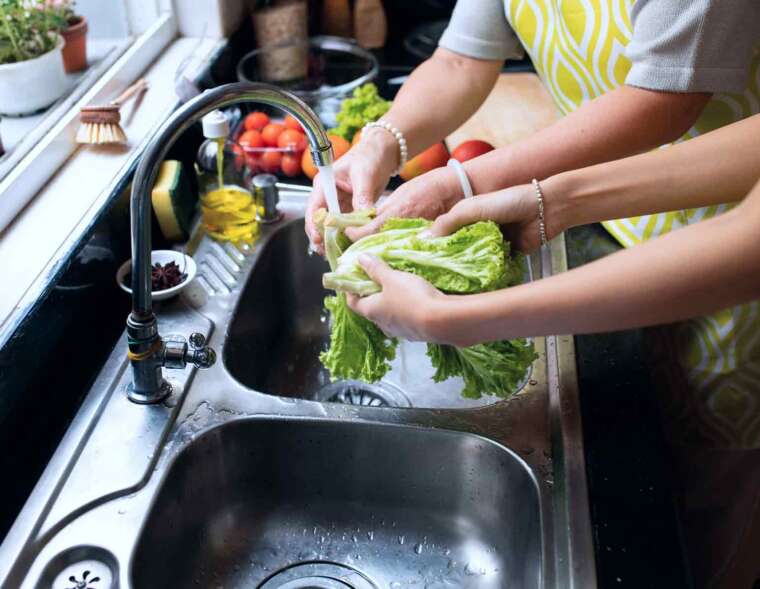 Two person bonding moment in the kitchen, washing vegetables together at the faucet