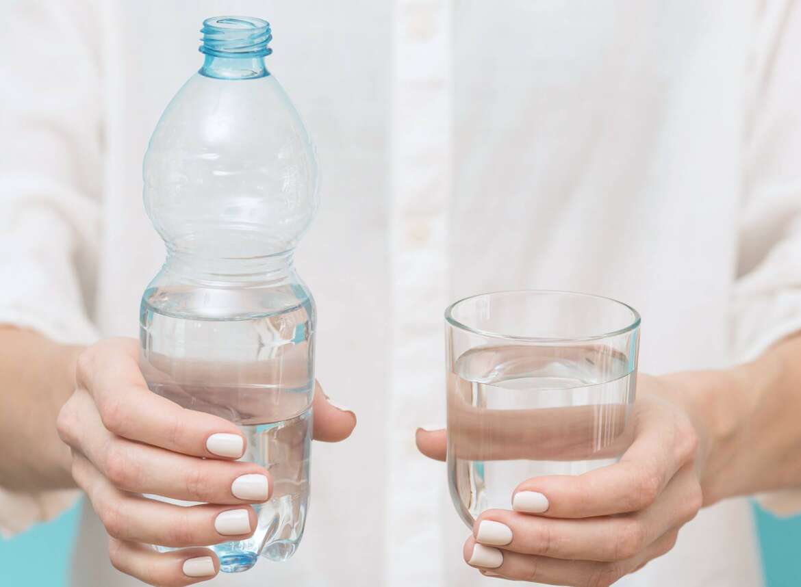 A person holding a glass of water and a bottle of water