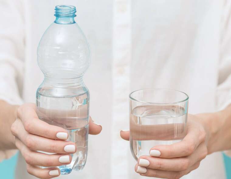 A person holding a glass of water and a bottle of water