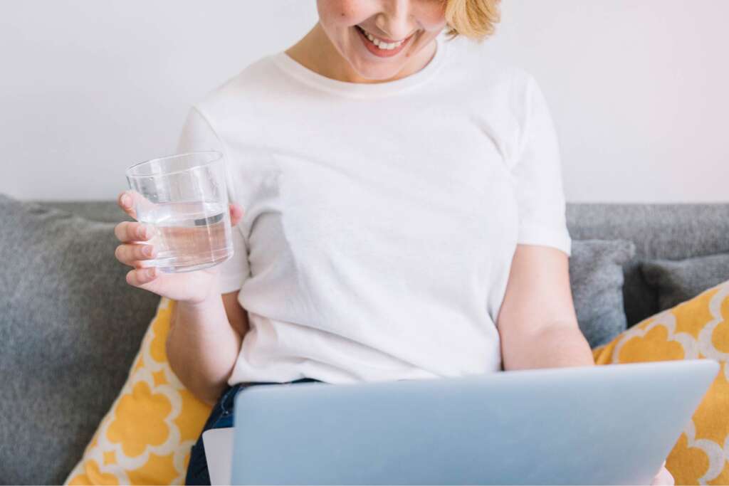 A woman enjoying a glass of iron-free well water while using her laptop