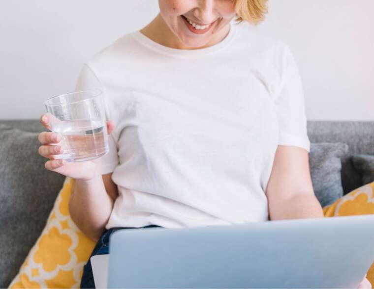 A woman enjoying a glass of iron-free well water while using her laptop