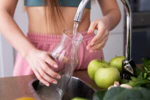 A woman filling a glass pitcher with water filtered through a reverse osmosis filtration system