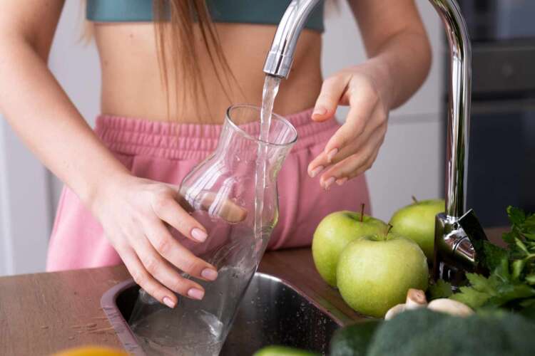 A woman filling a glass pitcher with water filtered through a reverse osmosis filtration system