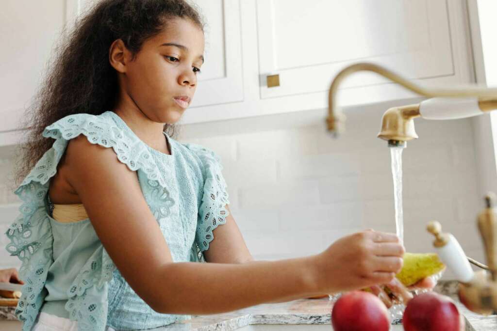 A young girl is washing fruits under running faucet water