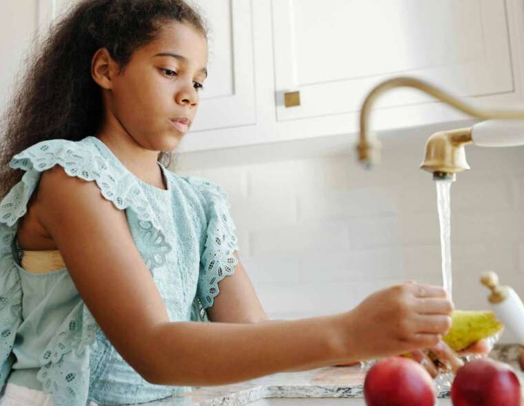 A young girl is washing fruits under running faucet water