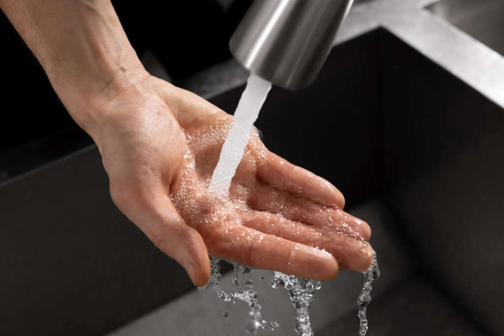 A hand is under freely flowing water in the sink