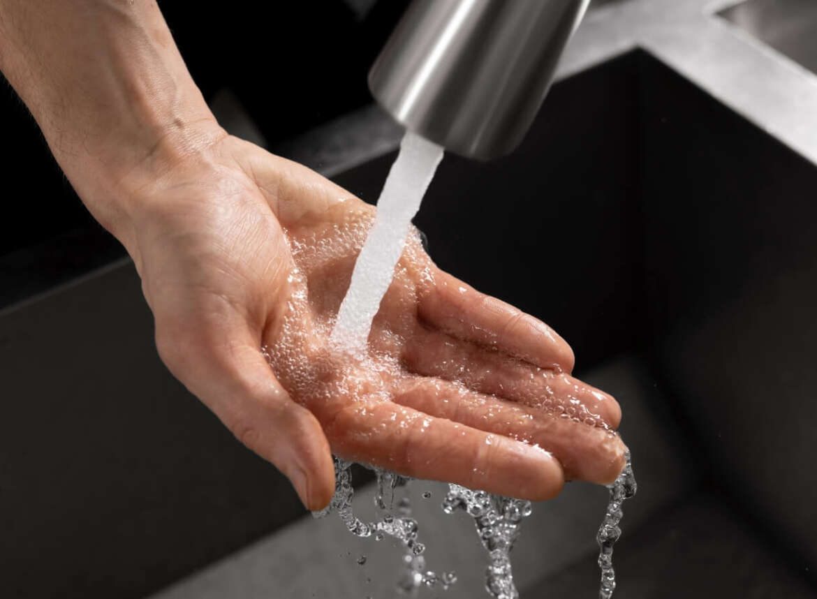 A hand is under freely flowing water in the sink
