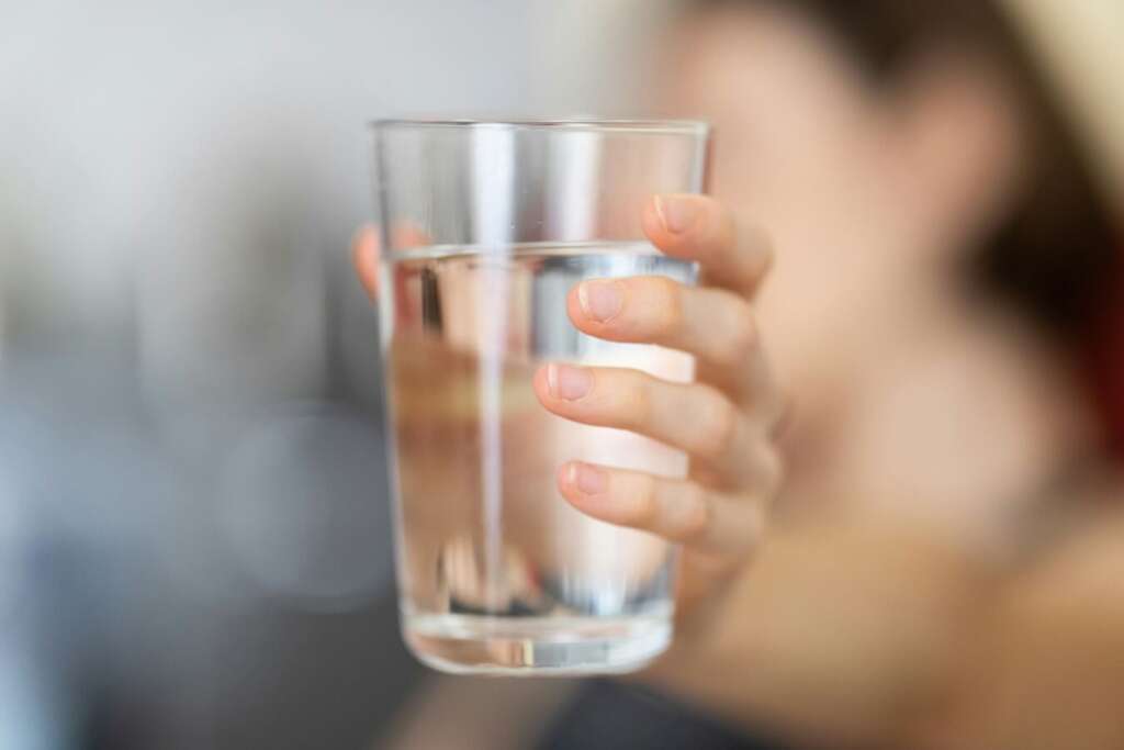 A hand holding a glass of water filtered through sediment filtration