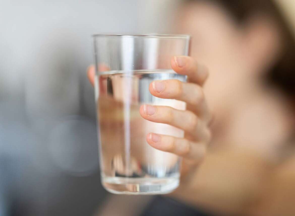 A hand holding a glass of water filtered through sediment filtration