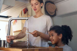 A woman washing a toothbrush at the sink while a girl watches