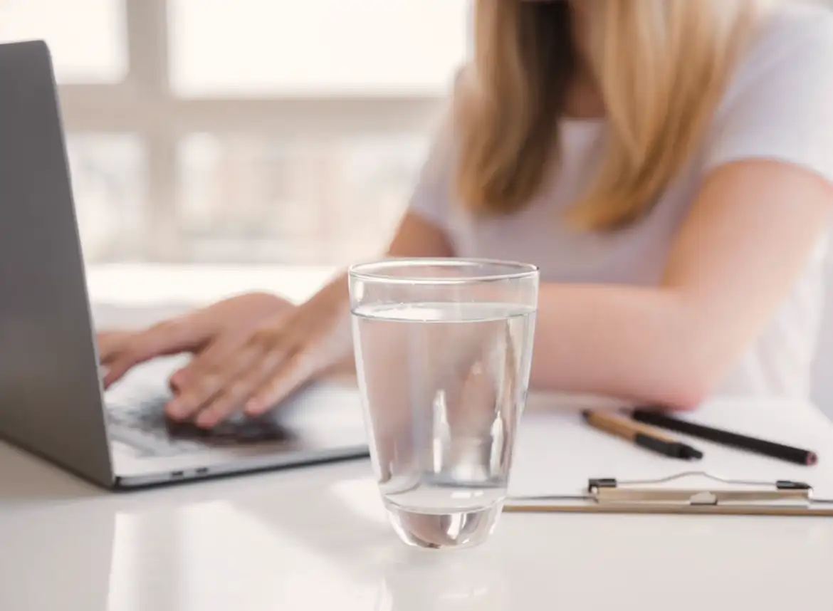 A woman working on her laptop with a glass of drinking water