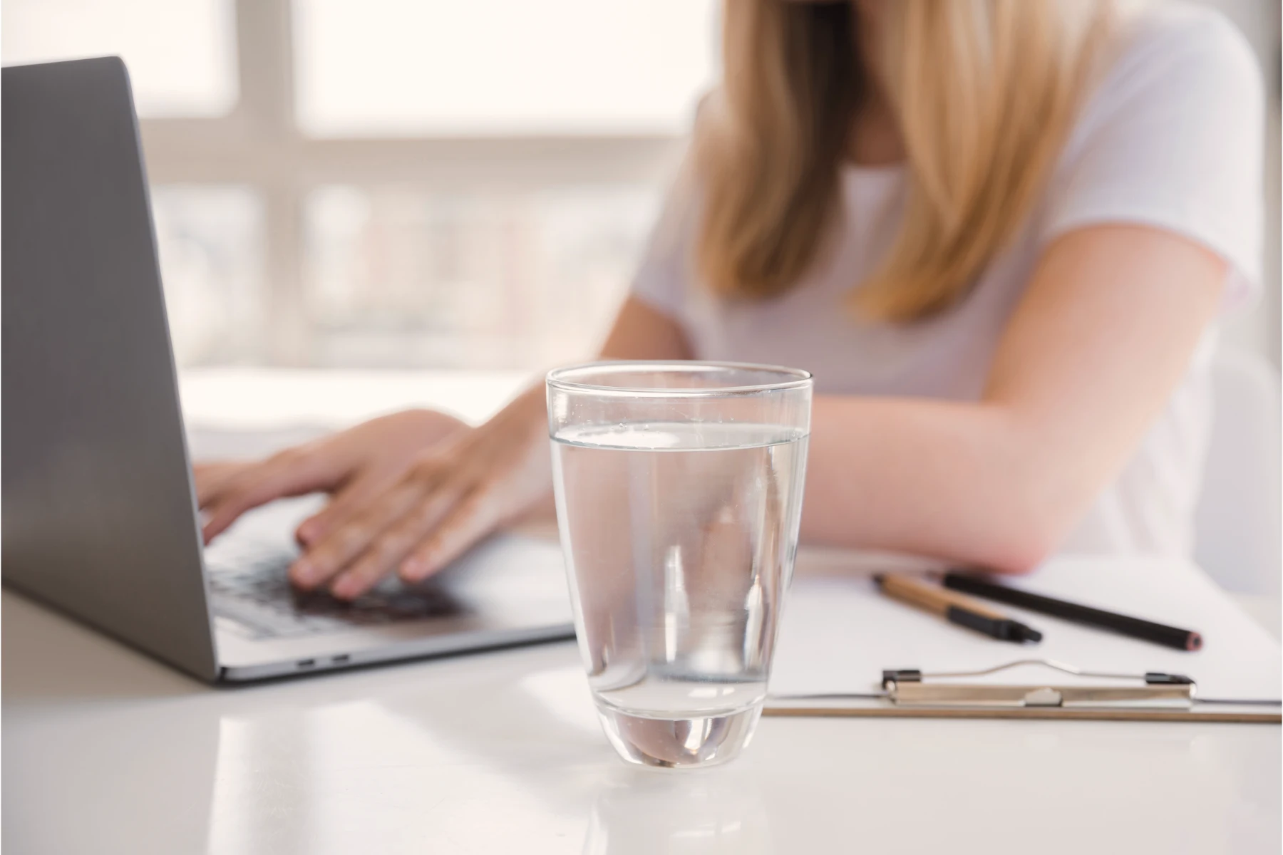 A woman working on her laptop with a glass of drinking water