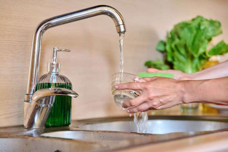 Person washing a bowl under running faucet water