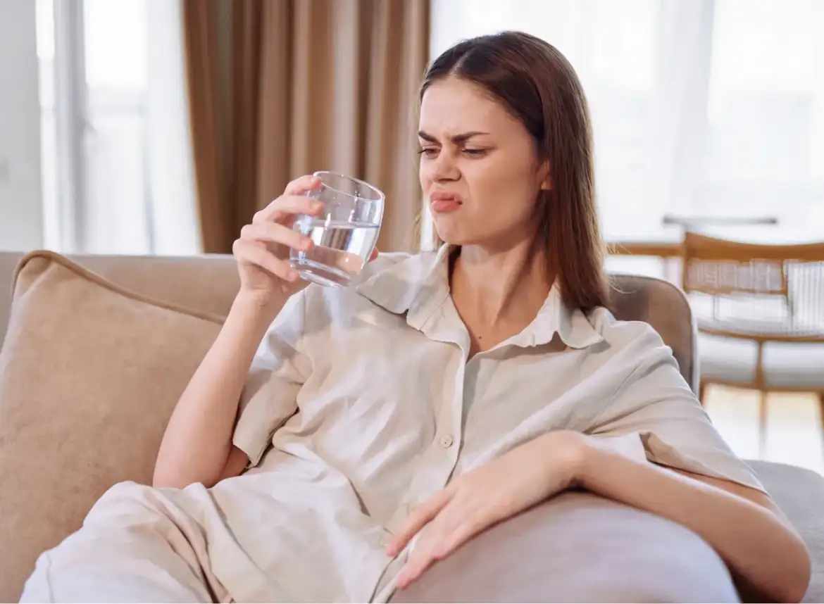 A woman smelling a glass of water that has a rotten-egg-like odor